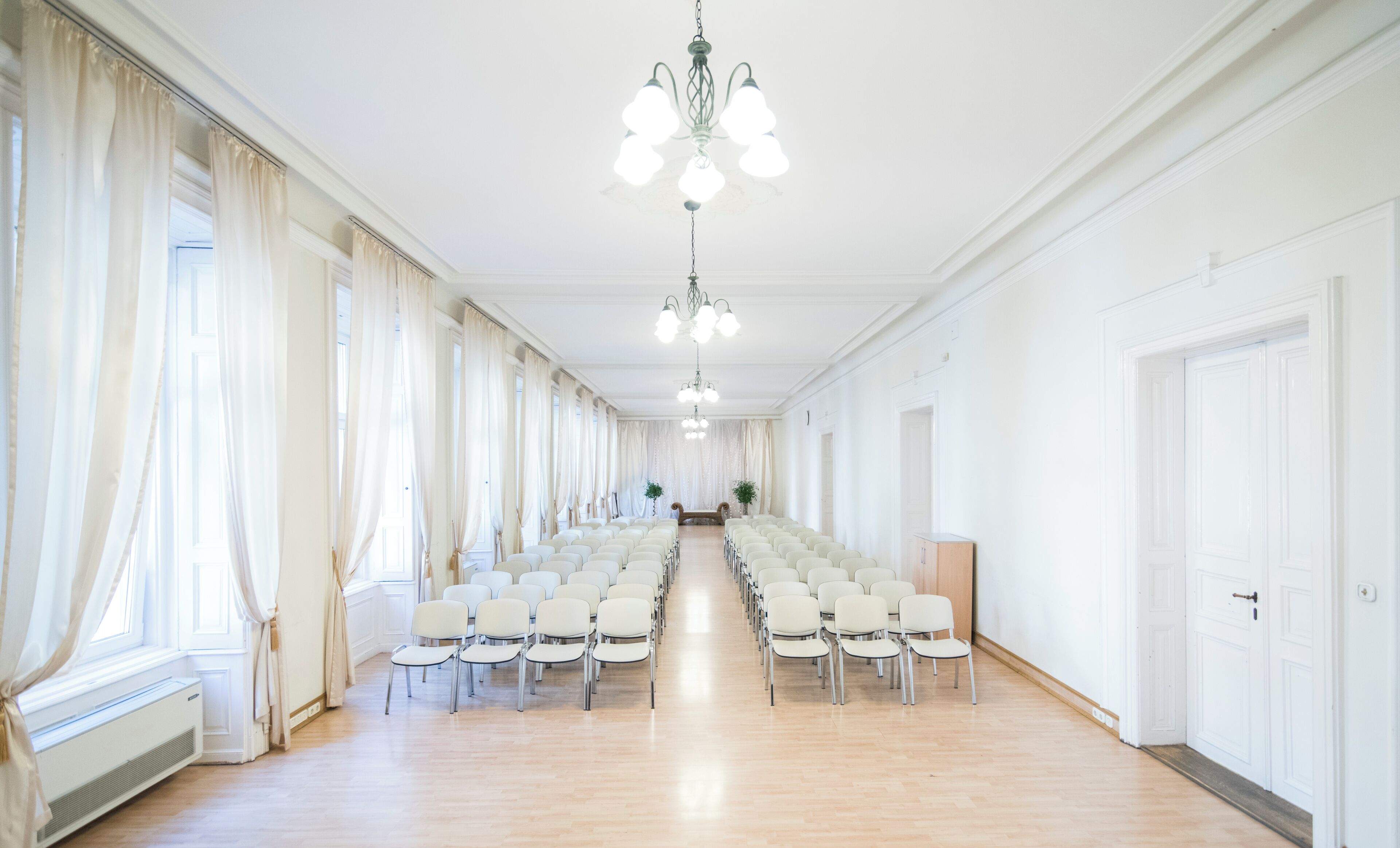 A long, narrow room with rows of chairs facing a central area with a chandelier.