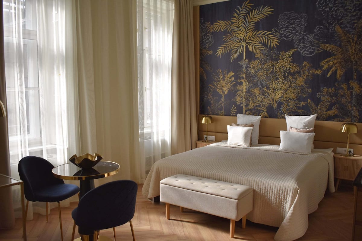Een hotelkamer met een groot bed, een ronde tafel met twee stoelen, een bankje en een wandtapijt.