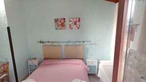 A bedroom with a bed, two nightstands, a chair, and two wall-mounted paintings. - Serraona triple room with bathroom (ALGHERO)