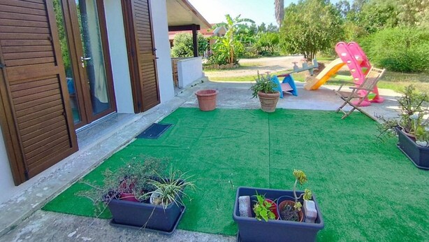 A modern house with a green artificial lawn, a wooden door, and a slide in the backyard. - Serraona triple room with bathroom (ALGHERO)