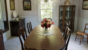 A dining room with a wooden table, chairs, a chandelier, and a vase of flowers.