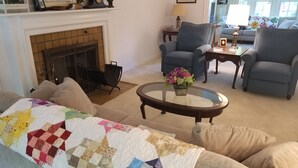 A cozy living room with a fireplace, a comfortable sofa, a coffee table with a vase of flowers, and a blue armchair.