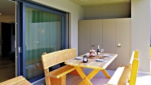 Un coin repas avec une table en bois dressée pour deux personnes, un banc et une porte-fenêtre coulissante donnant sur une autre pièce.