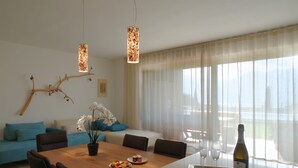 Un salon moderne avec une table à manger en bois, des coussins bleus, une plante en pot et une bouteille de vin posée sur un plateau.