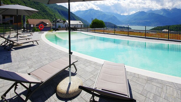 Un espace piscine doté de chaises longues et de parasols, entouré de montagnes et surplombant un ciel dégagé.