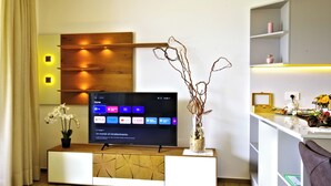 Un salon moderne avec un téléviseur à écran plat posé sur une console en bois, un vase décoré de branches et une étagère au design minimaliste.