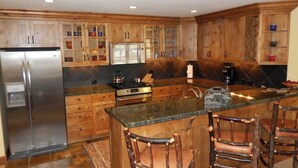 Una cocina con armarios de madera, un refrigerador de acero inoxidable, una estufa a gas y una barra con taburetes.