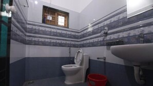 A bathroom with a toilet, a sink, and a red bucket. - Periyar Homes Deluxe Room 102 (Kumily)