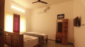 A single bed with a wooden headboard, a bedside table, a mirror, and a television mounted on the wall. - Periyar Homes Deluxe Room 102 (Kumily)