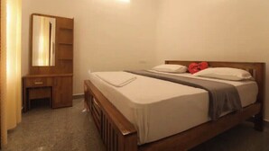 A bedroom with a wooden bed, a bedside table, a mirror, and a wardrobe. - Periyar Homes Deluxe Room 102 (Kumily)