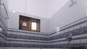 A small bathroom with a toilet, a red bucket, and a showerhead. - Periyar Homes Deluxe Room 102 (Kumily)