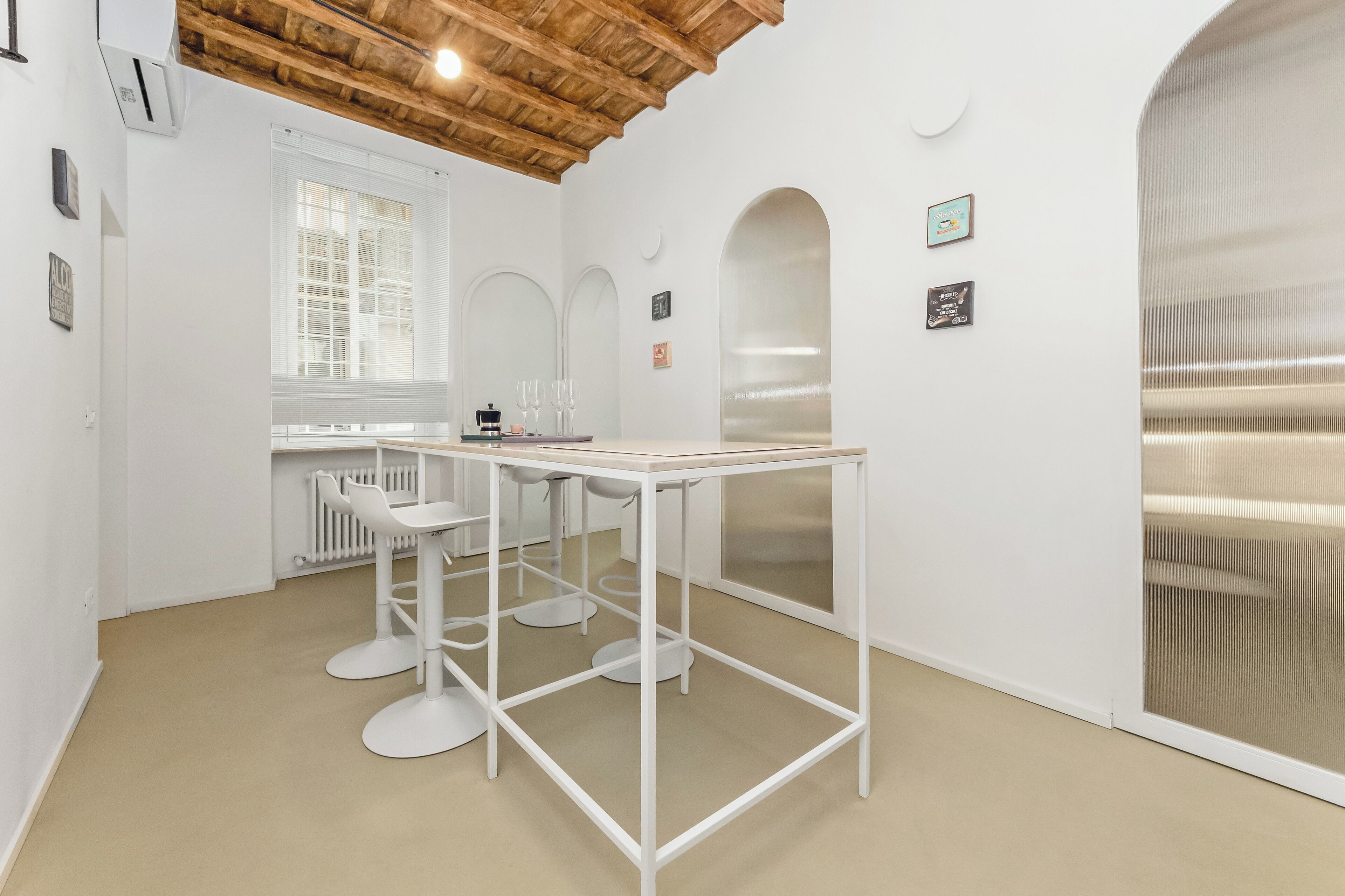 A modern, minimalist room with a white table and chairs, a wooden ceiling, and a large window.