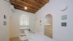 Une pièce avec une table blanche, des chaises blanches, un plafond en bois et une fenêtre avec des stores.