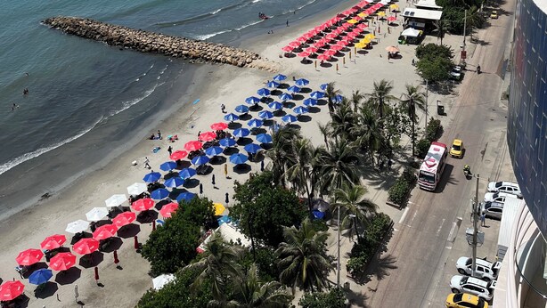 Un paysage urbain côtier avec une plage bordée de parasols colorés, une promenade et des bâtiments modernes.