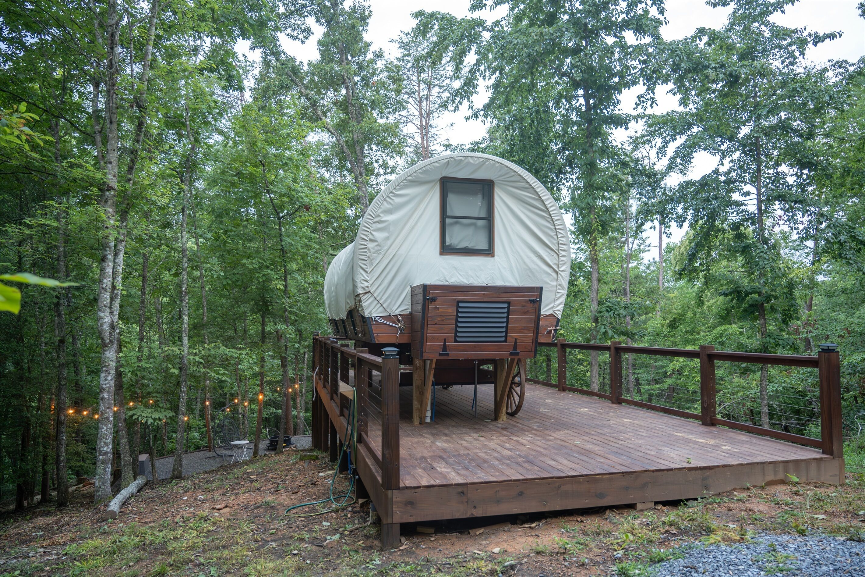 Un lit en bois, abrité, situé dans une zone boisée, avec une terrasse en bois et une rambarde.