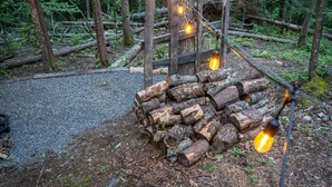 A rustic outdoor area with a pile of logs, a wooden fence, and string lights.