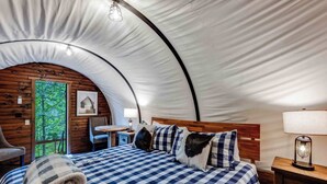 A tented accommodation with a checkered bed, wooden walls, a small table, and a chair.