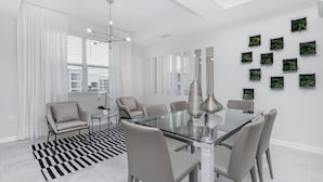 A modern dining area with a glass table, grey chairs, and a black and white striped rug.