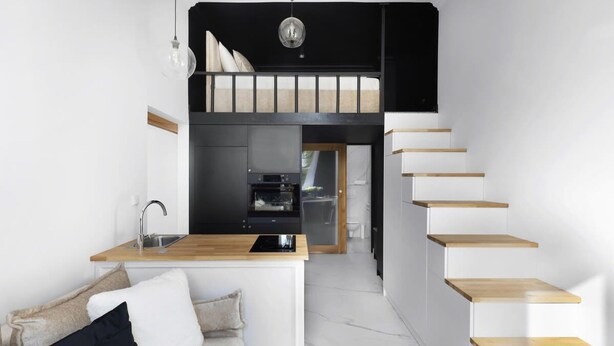 Ein kompaktes, modernes Apartment mit Küchenzeile, einer Couch und einer Holztreppe.