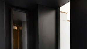 Ein modernes, minimalistisches Zimmer mit dunkler Wand, einer Holzbank und einem großen Spiegel.