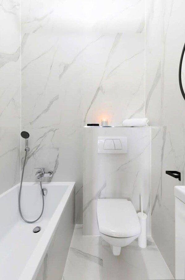 A modern bathroom with a marble wall, a white bathtub, a toilet, and a showerhead. - Elite Apartments Ogarna B W View of the old Town Free Internet OLD Town (Gdansk)