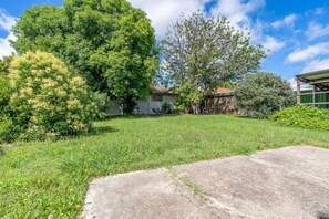Stroll through the beautifully manicured lawn surrounded by mature trees, including a large tree and a smaller one, and enjoy the covered porch area.