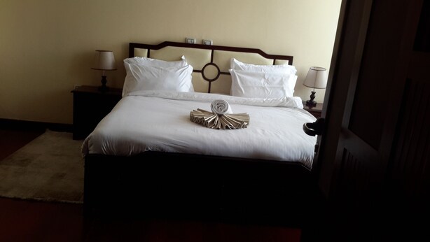 Una cama bien hecha con ropa blanca, dos almohadas y una toalla decorativa. Hay dos mesitas de noche con lámparas.