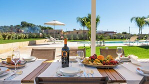 Un espace de restauration en plein air avec vue sur la piscine, une bouteille de vin et un assortiment de fruits.