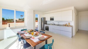 Une cuisine moderne avec des meubles blancs, un réfrigérateur en acier inoxydable et un coin repas comprenant une table en bois et des chaises bleues.