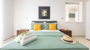 Un lit bien fait, avec une literie verte et jaune, une pile de serviettes blanches et un chapeau de paille posé sur le lit.