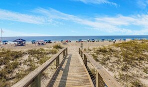 Une promenade en bois menant à une plage où se trouvent des parasols et des chaises de plage.