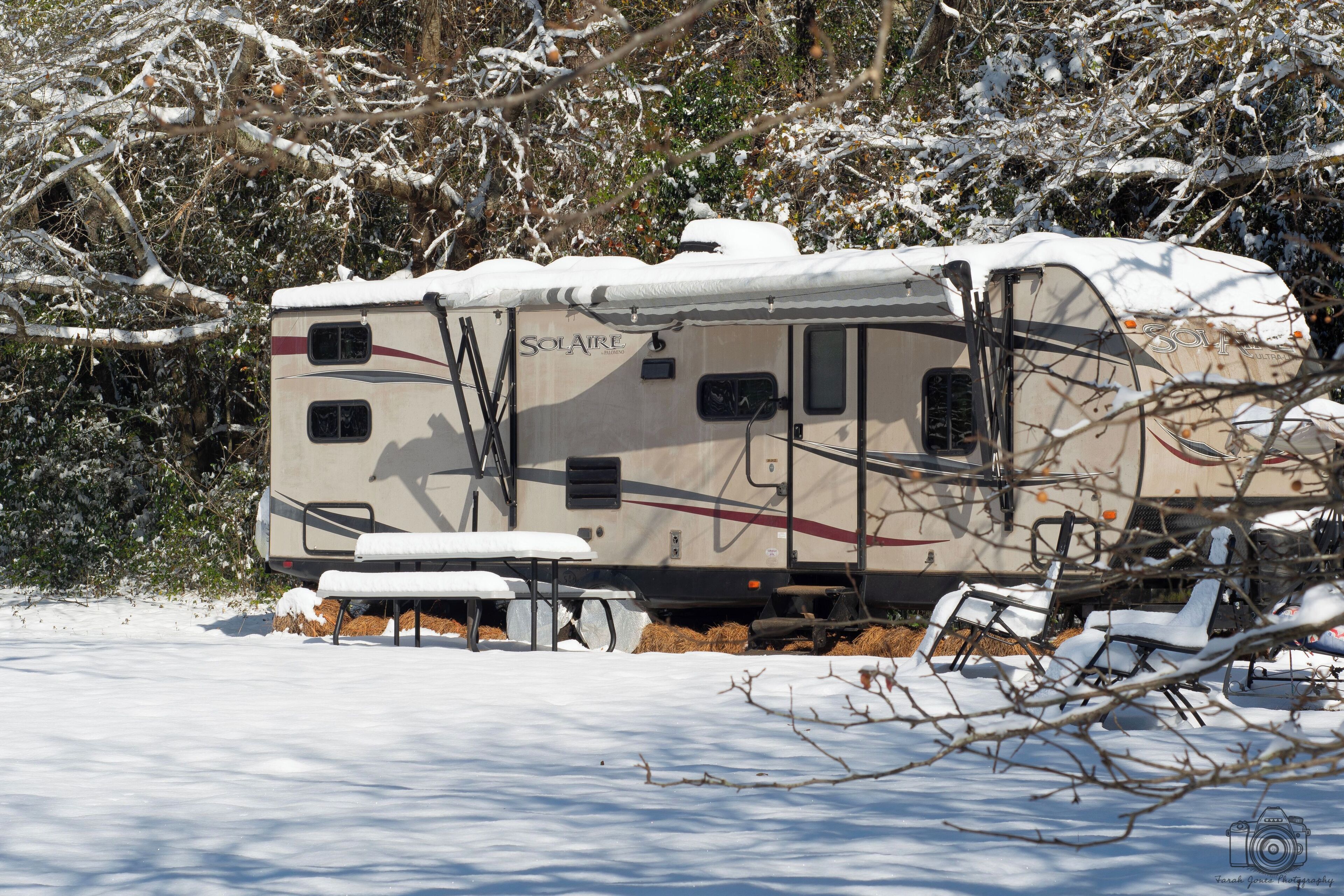 Un camper ricoperto di neve con il logo "SOLATRE", circondato da alberi e neve.