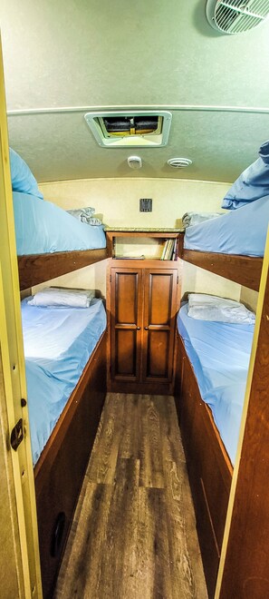 A narrow cabin with bunk beds, wooden walls, and a central door. - Cozy Camper 2-bedroom RV in Americus GA (Americus)