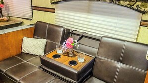 A cozy RV interior with a leather sofa, a small table with a vase, and wooden cabinets. - Cozy Camper 2-bedroom RV in Americus GA  (Americus)
