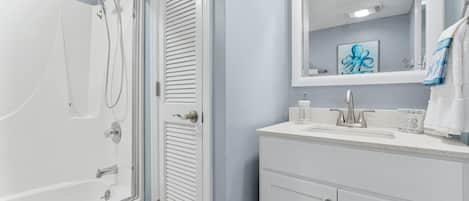 Un baño con ducha, lavamanos y espejo.