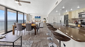 A modern kitchen with a large island, a dining area with a view, and a ceiling fan. - Sandpiper Beacon Beach Resort (Panama City Beach)