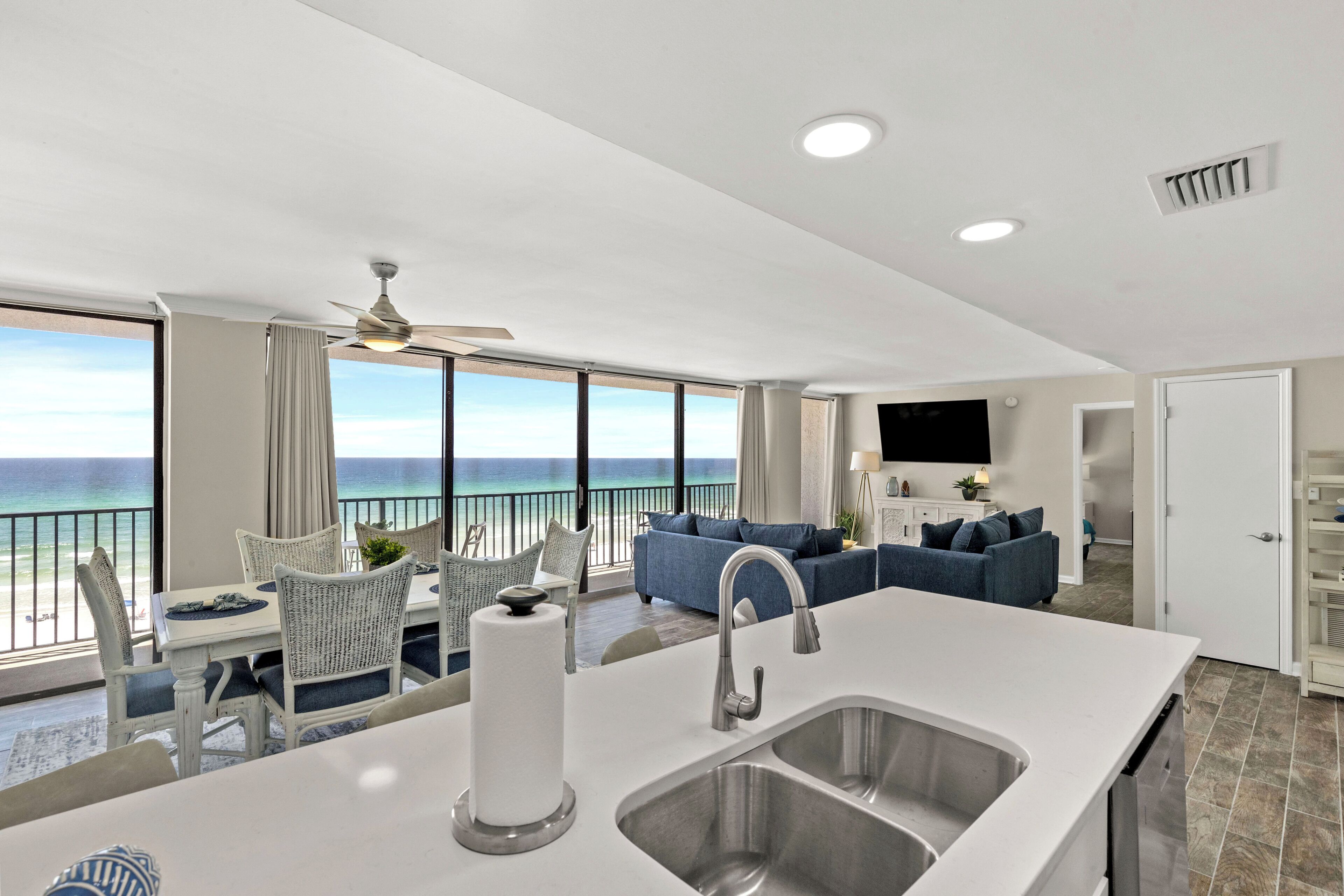 Una cucina moderna con un'isola grande, un'area pranzo con sedie in vimini e vista sull'oceano.