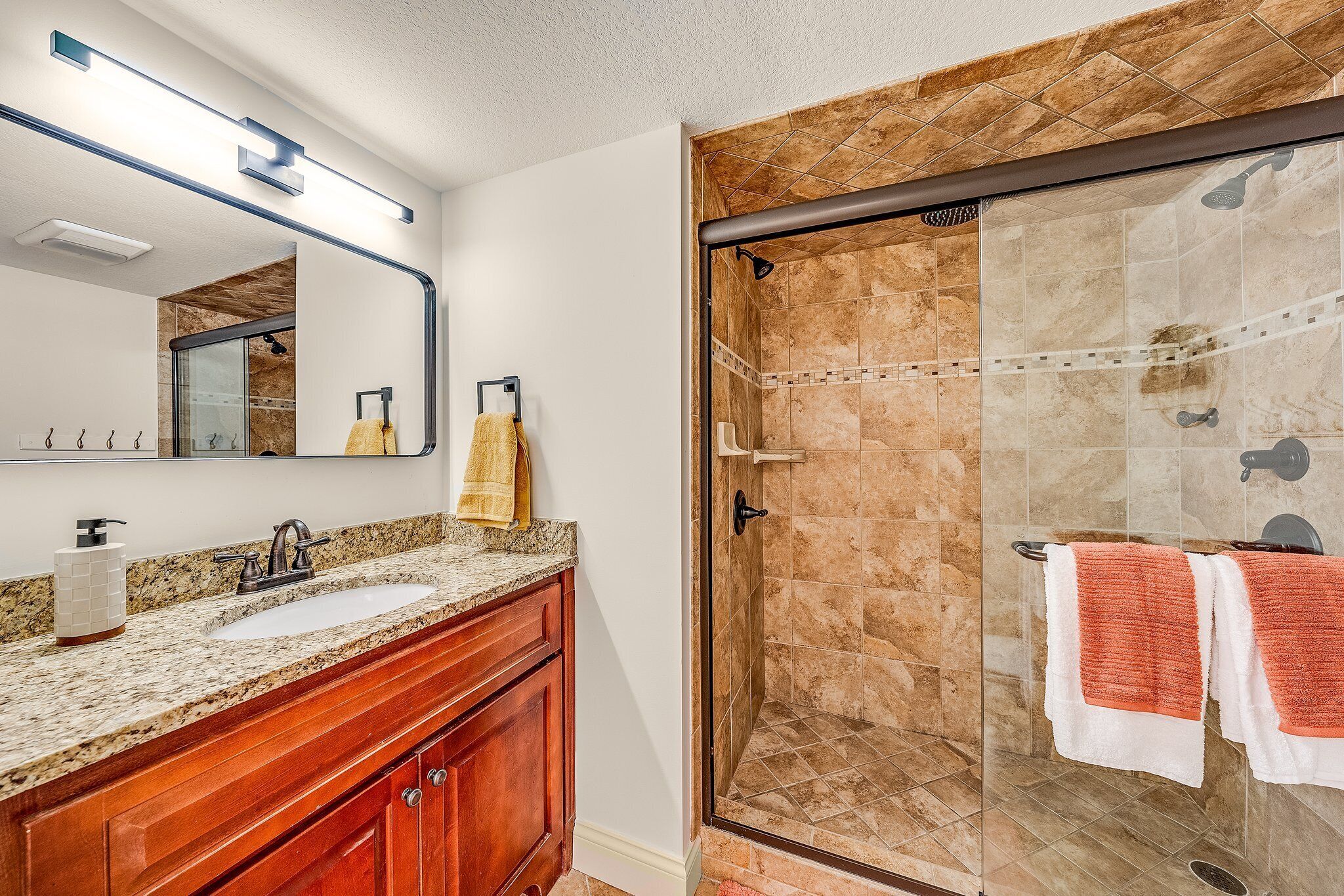 Un baño con lavamanos de encimera de granito, tocador de madera y mampara de ducha con suelo de azulejos.
