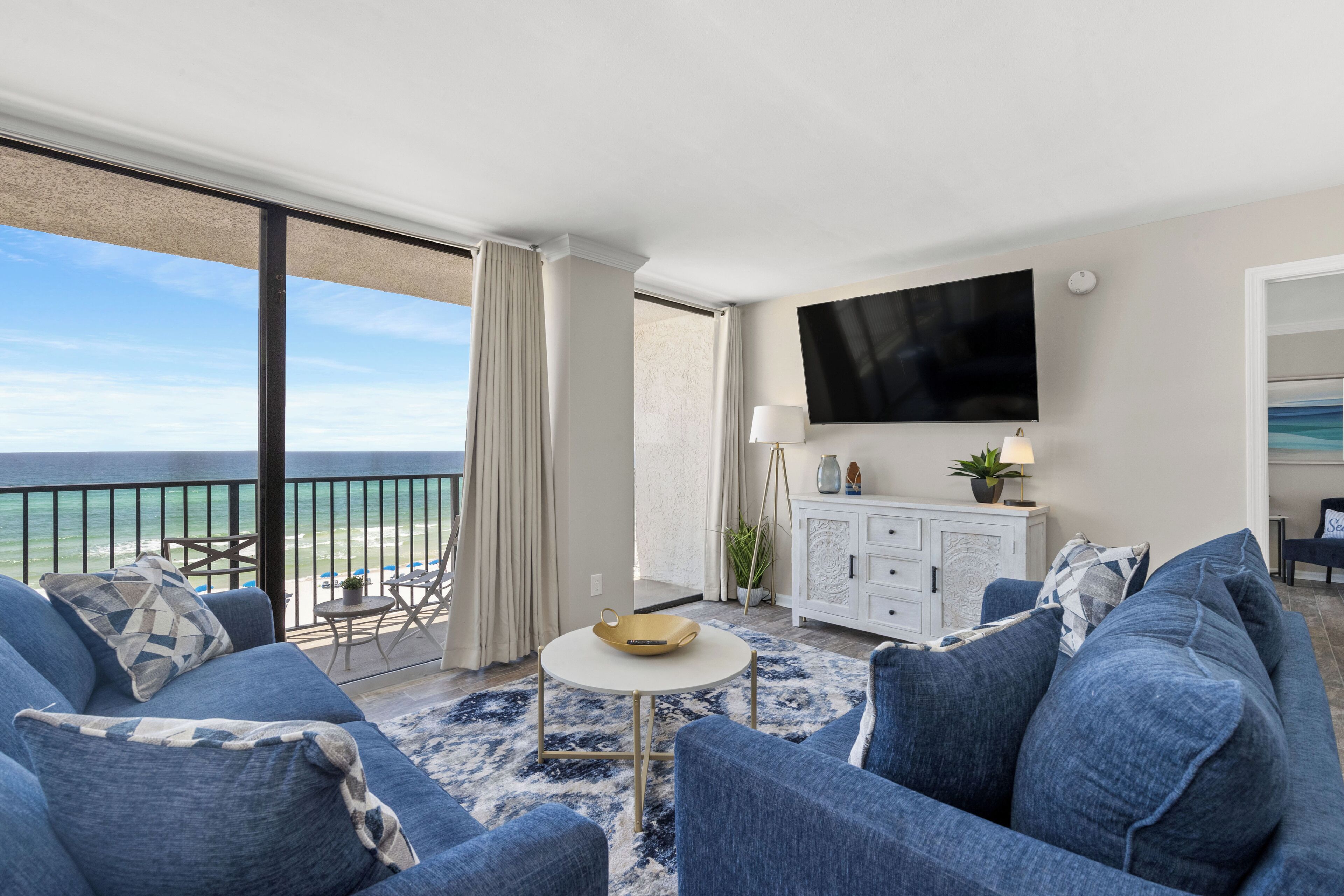 Una habitación de hotel moderna con balcón y vistas al océano, un televisor de pantalla plana montado en la pared y una consola blanca con lámpara.