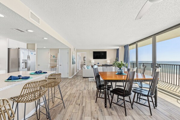 Una cocina moderna con una isla grande, un comedor con mesa y sillas de madera, y un balcón con vista al océano.