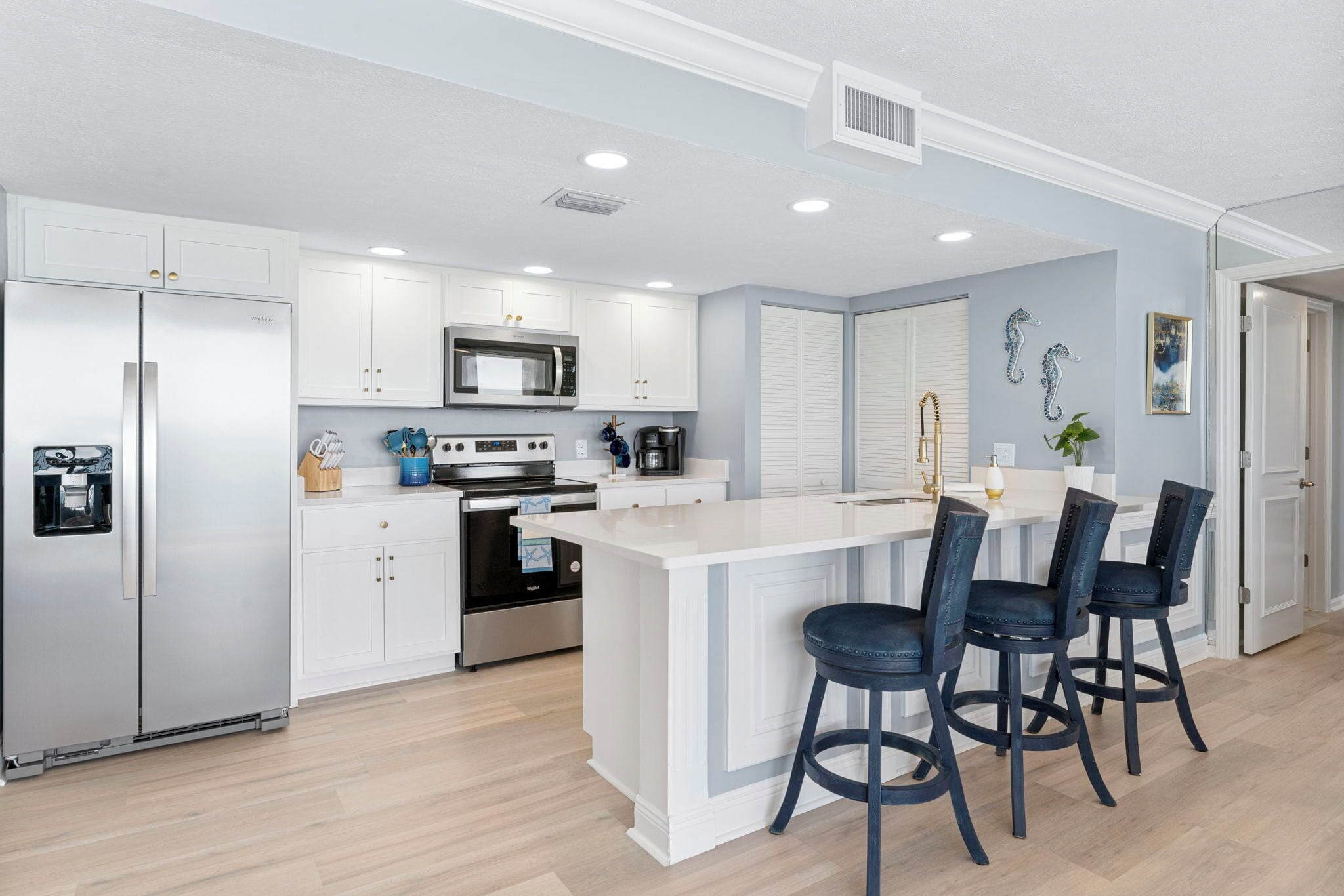 A modern kitchen with white cabinetry, stainless steel appliances, and a central island with bar stools.