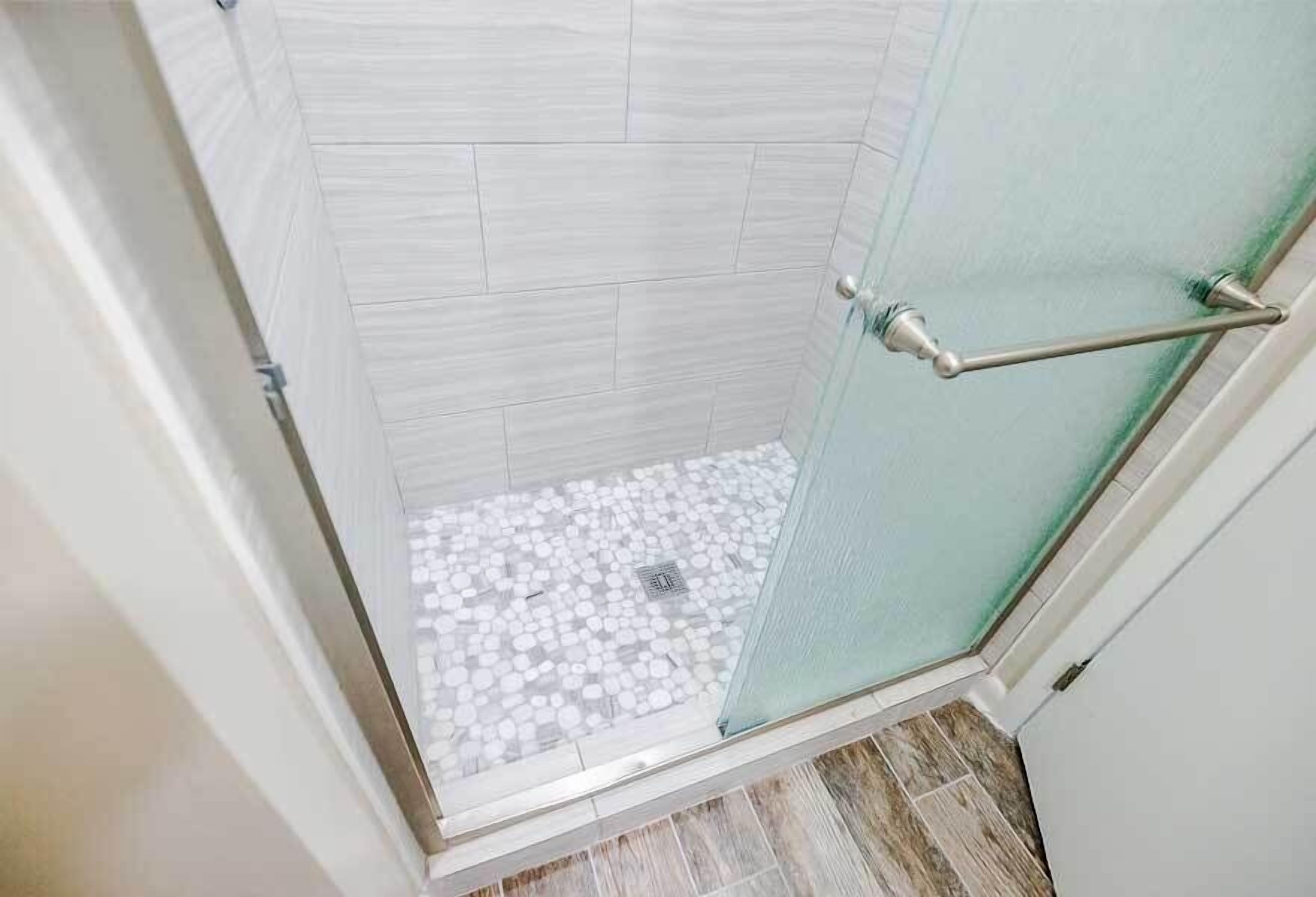 A shower with a glass door, tiled walls, and a floor with small white tiles.