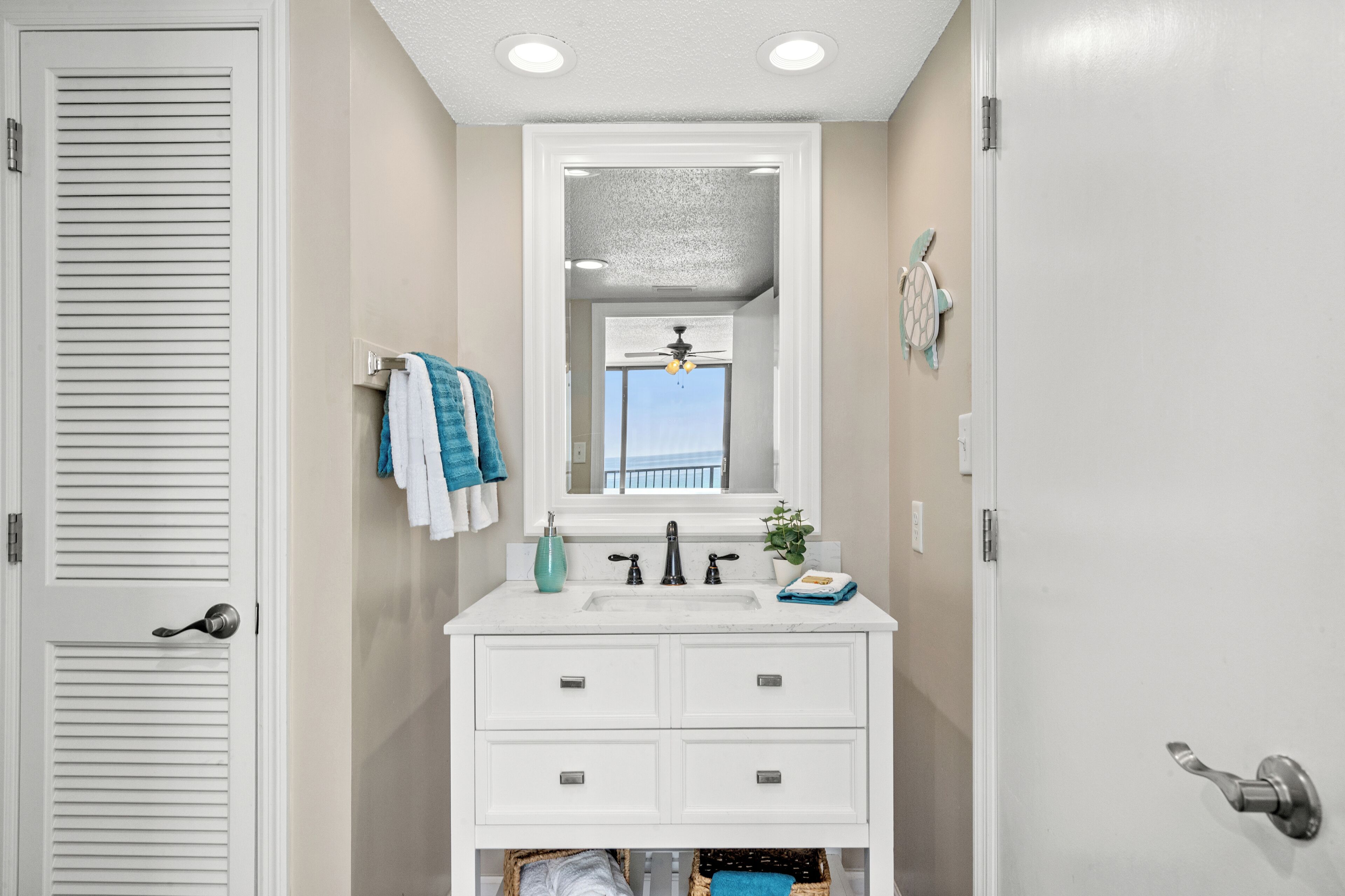 A bathroom with a white vanity, a large mirror, and a ceiling fan.