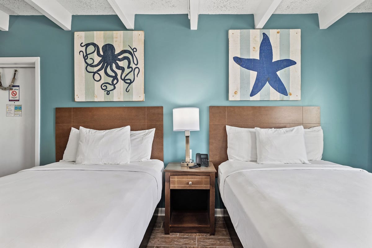 Una habitación de hotel con dos camas, una mesita de noche con lámpara y obras de arte en las paredes.