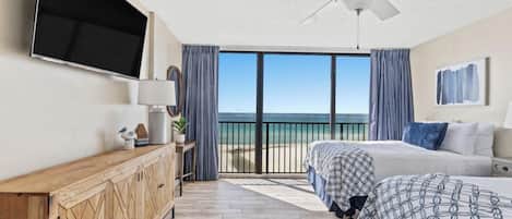 A bedroom with a large bed, a ceiling fan, a TV, and a view of the ocean.