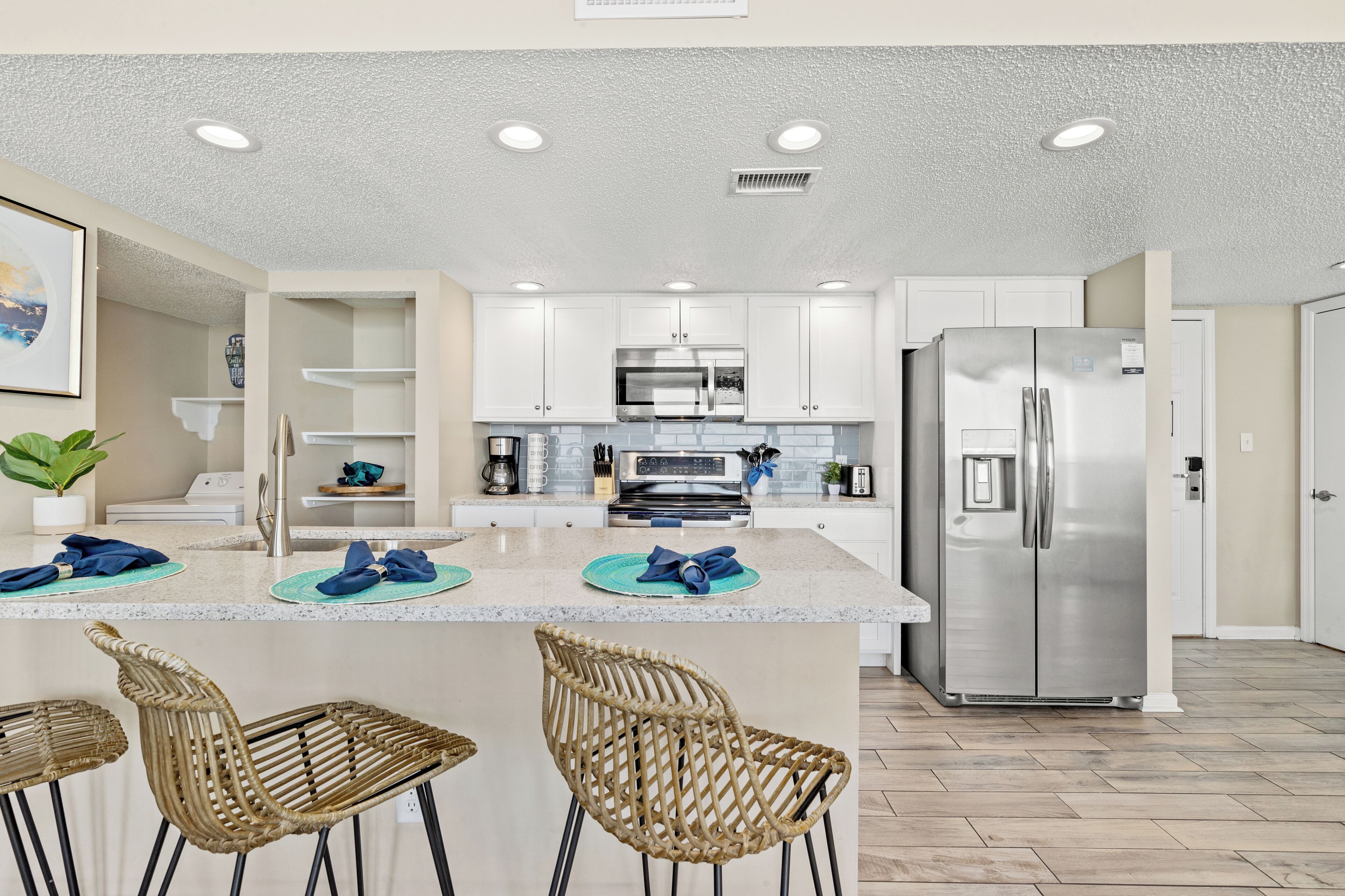 Una cocina moderna con muebles blancos, electrodomésticos de acero inoxidable y una isla central con taburetes de bar.