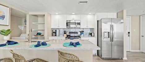 Una cocina moderna con muebles blancos, electrodomésticos de acero inoxidable y una isla central con taburetes de bar.