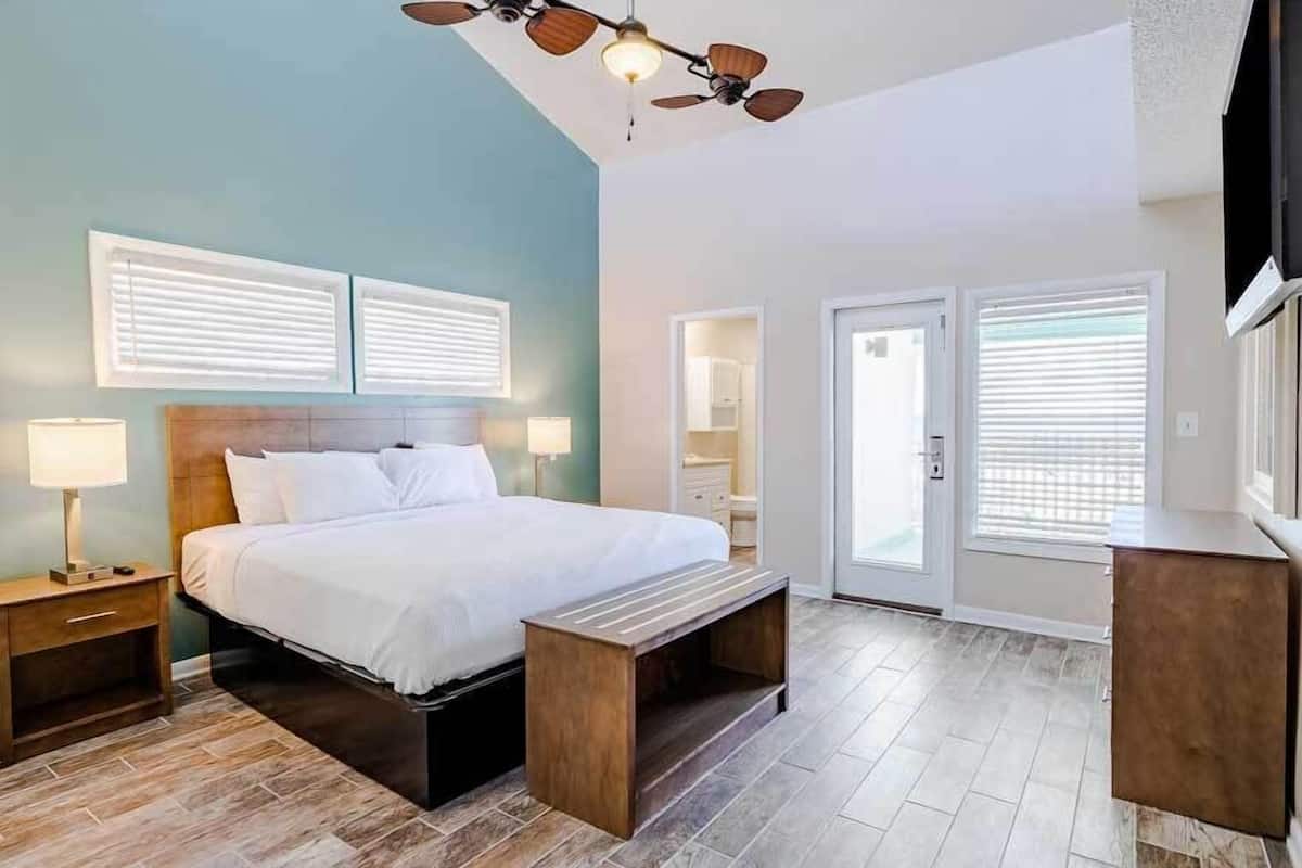 Un dormitorio con cama, mesitas de noche, ventilador de techo y vistas al baño a través de una puerta abierta.