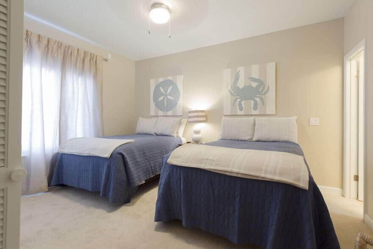 Un dormitorio con dos camas, paredes color beige y una lámpara en el techo.