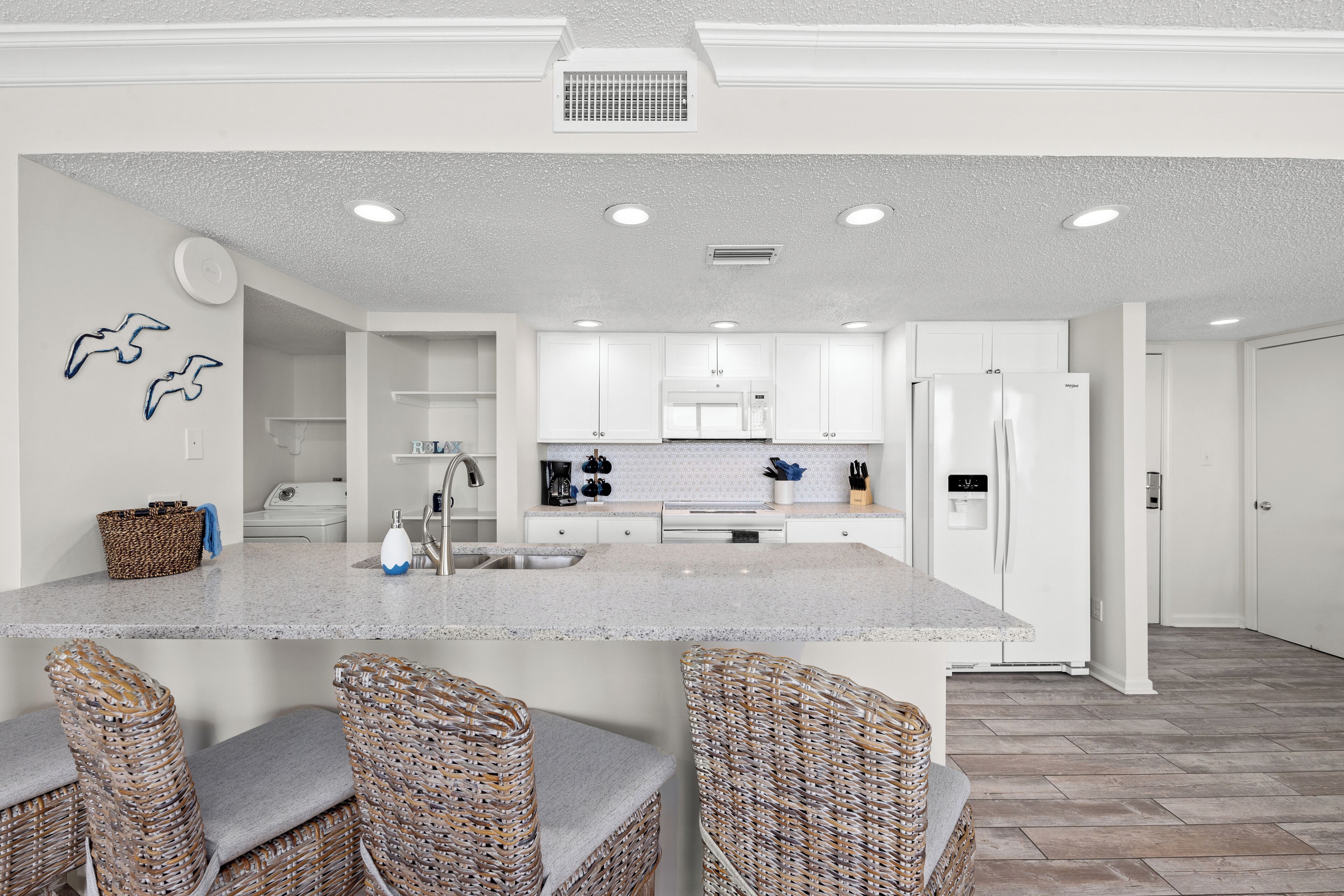 A modern kitchen with white cabinetry, a central island with bar stools, and a microwave.